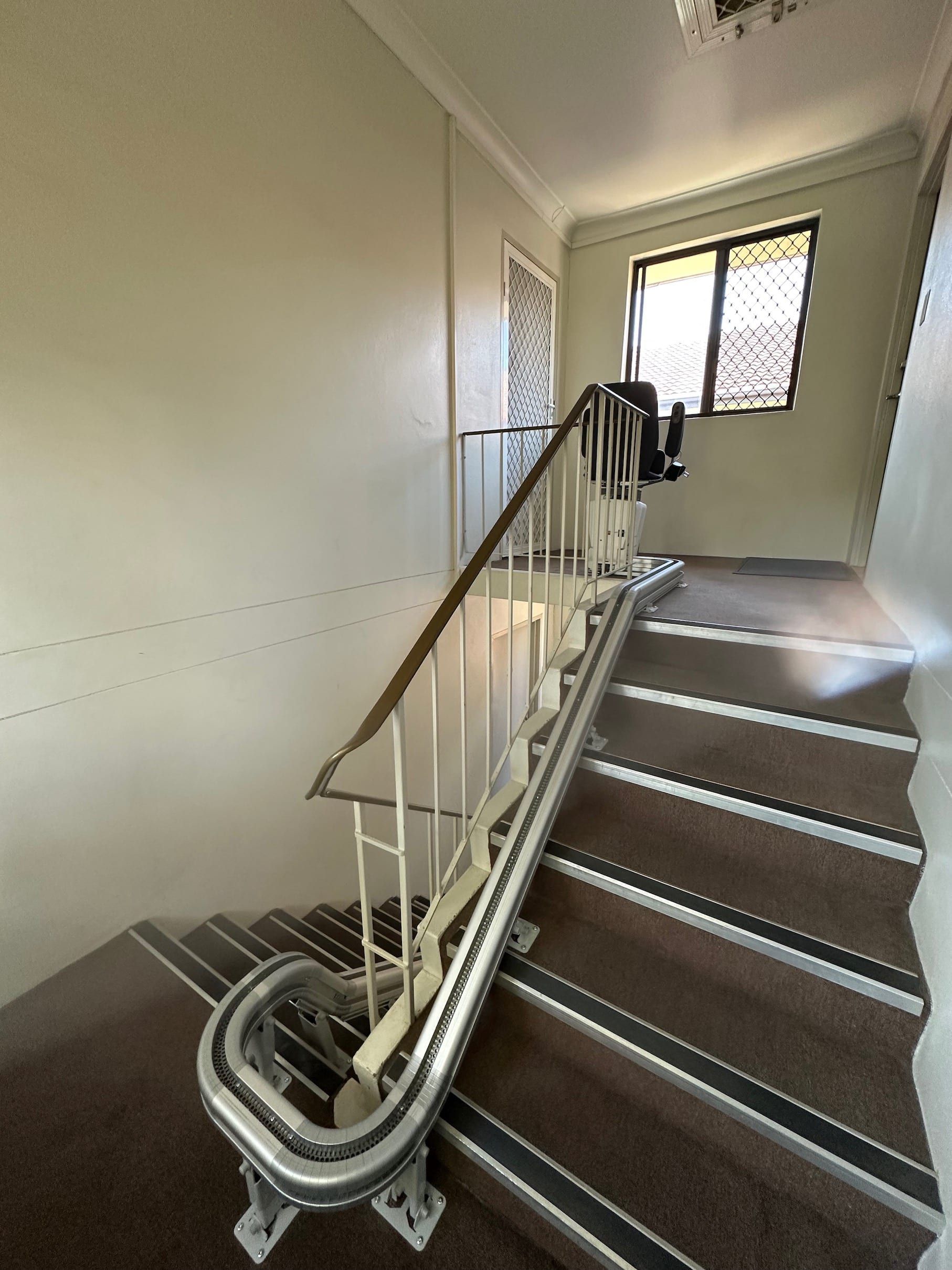 Indoor stairway with a stairlift rail running up the steps beside a window