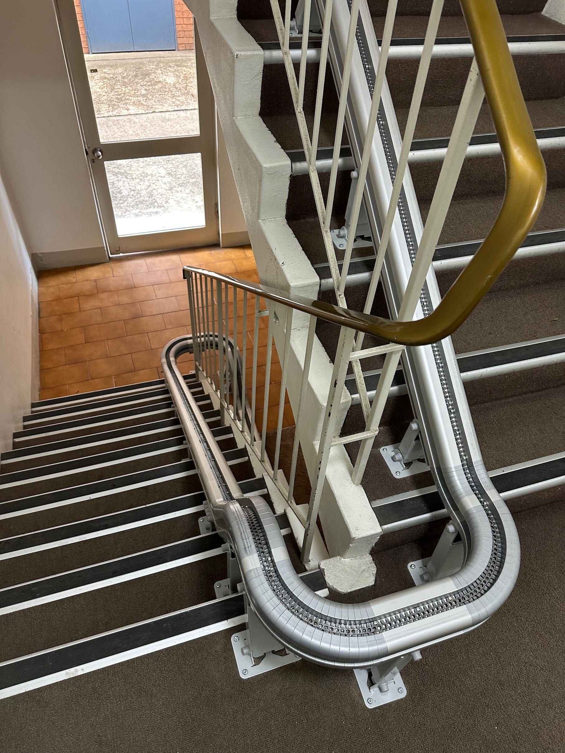 Stairwell with a curved white stairlift track and yellow handrail beside carpeted stairs.