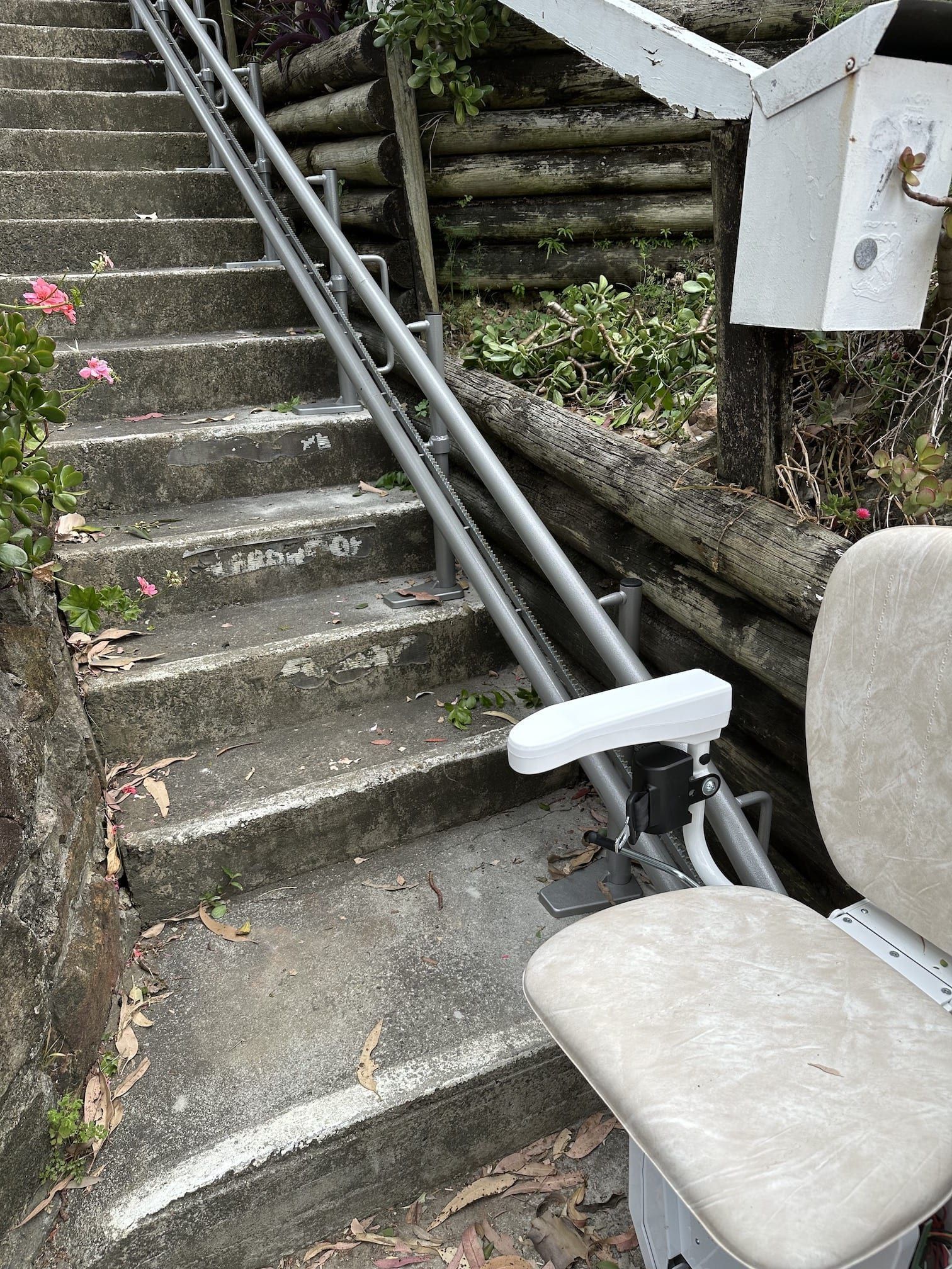 Outdoor stairs with metal handrails and an attached stair lift chair beside the steps