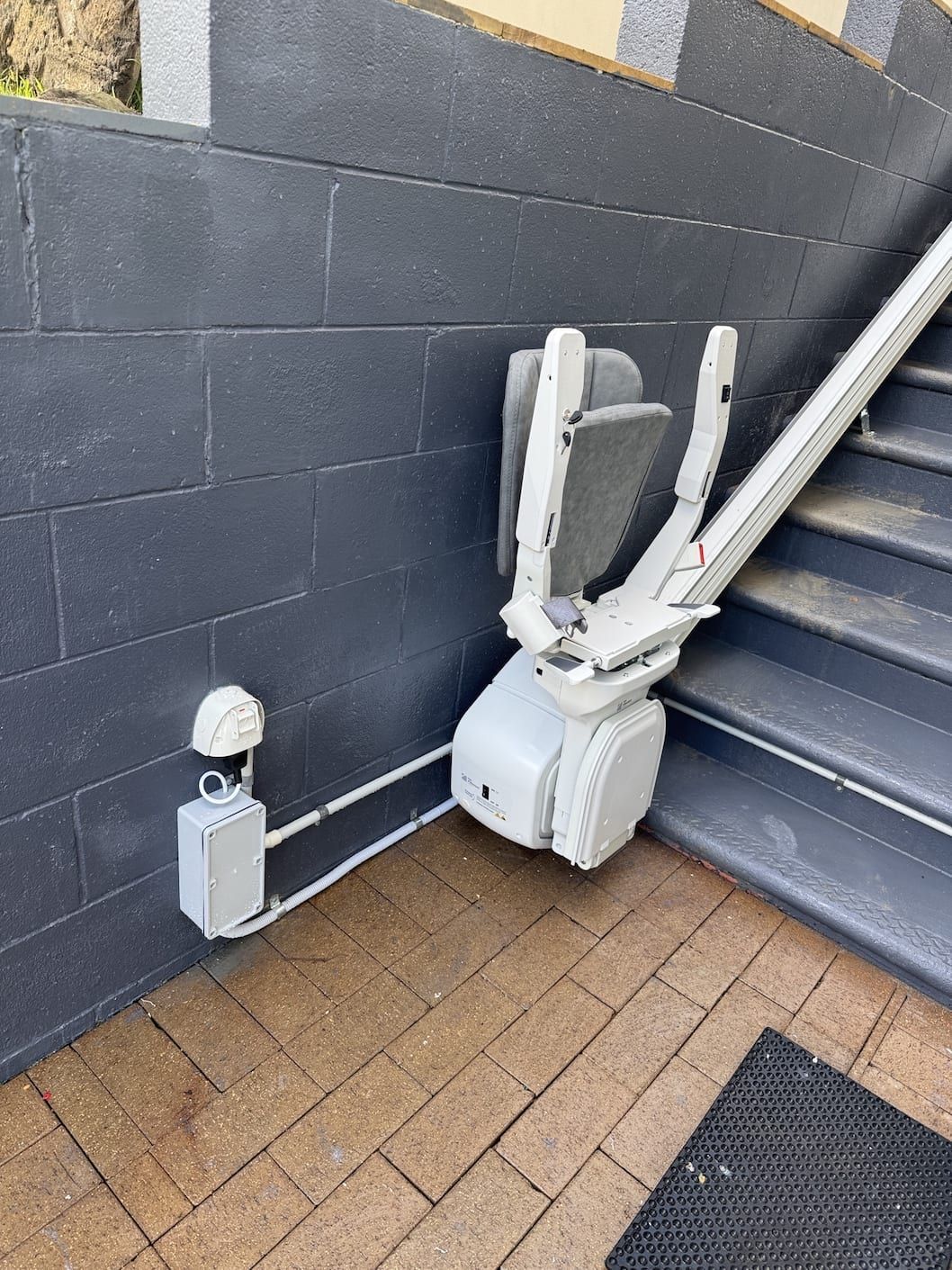 A white, motorized curved stairlift parked at the base of wooden stairs in a home.