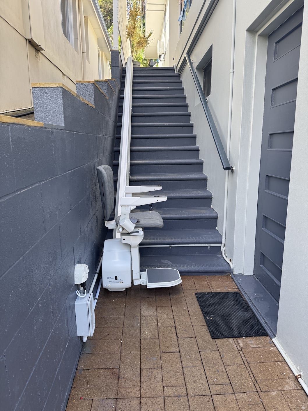 A blue upholstered stairlift chair with armrest controls, positioned on a rail alongside a wall.