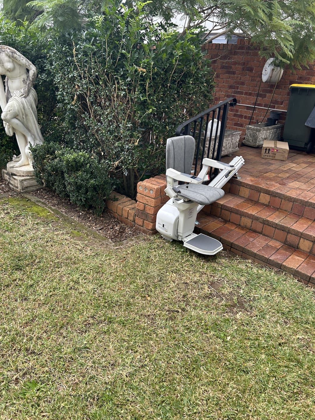 White stairlift on brick steps beside a garden and lawn