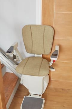 Indoor stairlift chair with beige seat and backrest on a staircase.