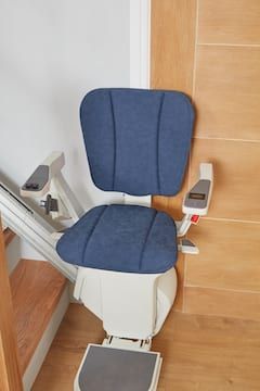 Blue stair lift chair beside a wooden staircase, mounted on the stair rail