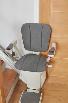 Gray stair lift chair on a staircase beside a wooden door and white wall.
