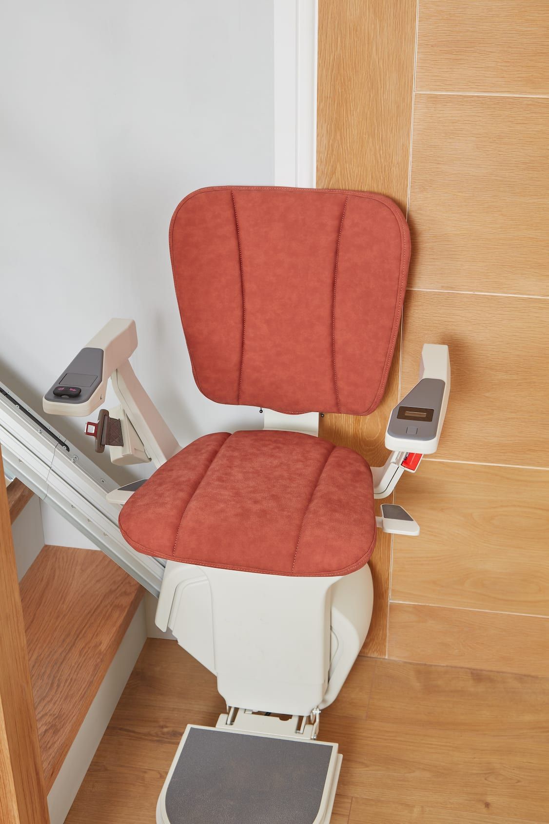 Red upholstered stair lift chair beside wooden stairs and wall paneling