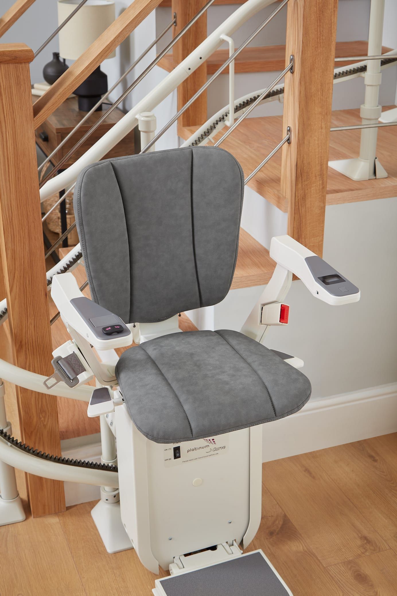 Gray stairlift chair on a staircase with white railings and wooden banister