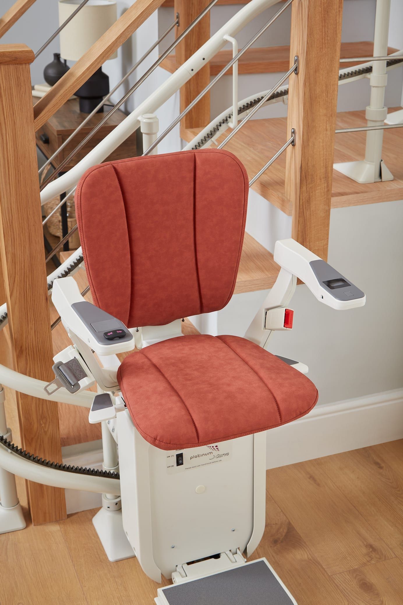 Red stairlift chair with orange upholstery on a curved staircase indoors.