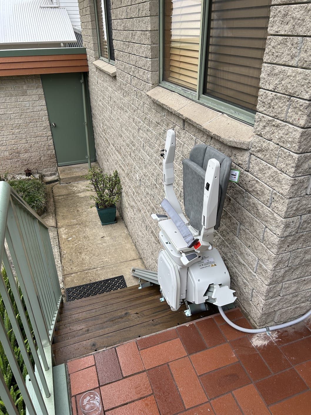A person sitting in a stairlift, wearing a grey seatbelt secured by a red buckle.