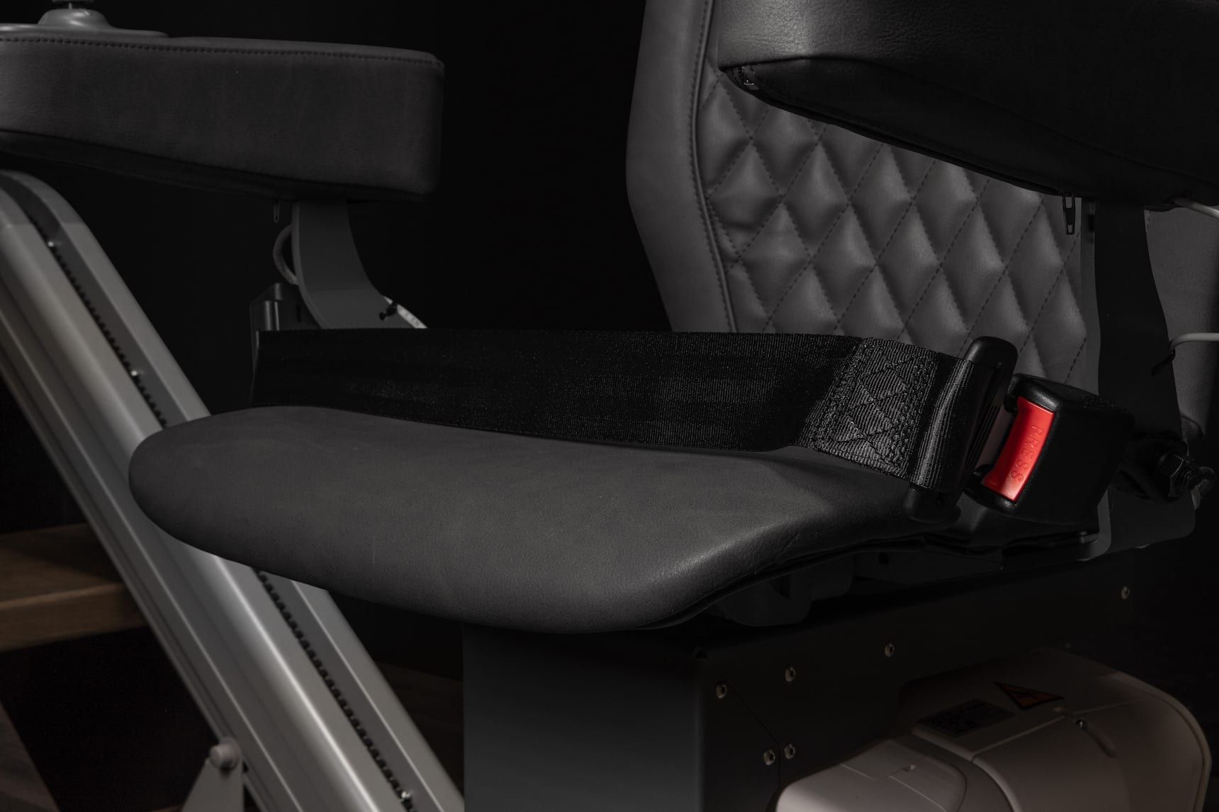 Padded black seat cushion with straps mounted inside a vehicle or wheelchair-like frame