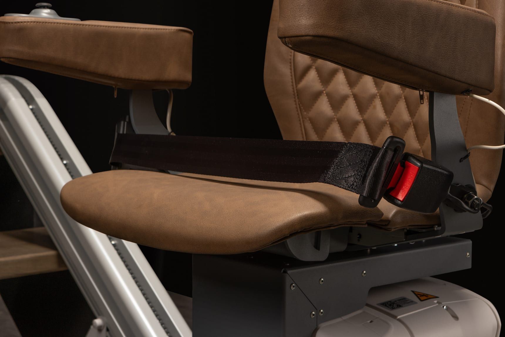 Close-up of a tan padded seat with a black-and-red seatbelt in a simulator or machinery cabin