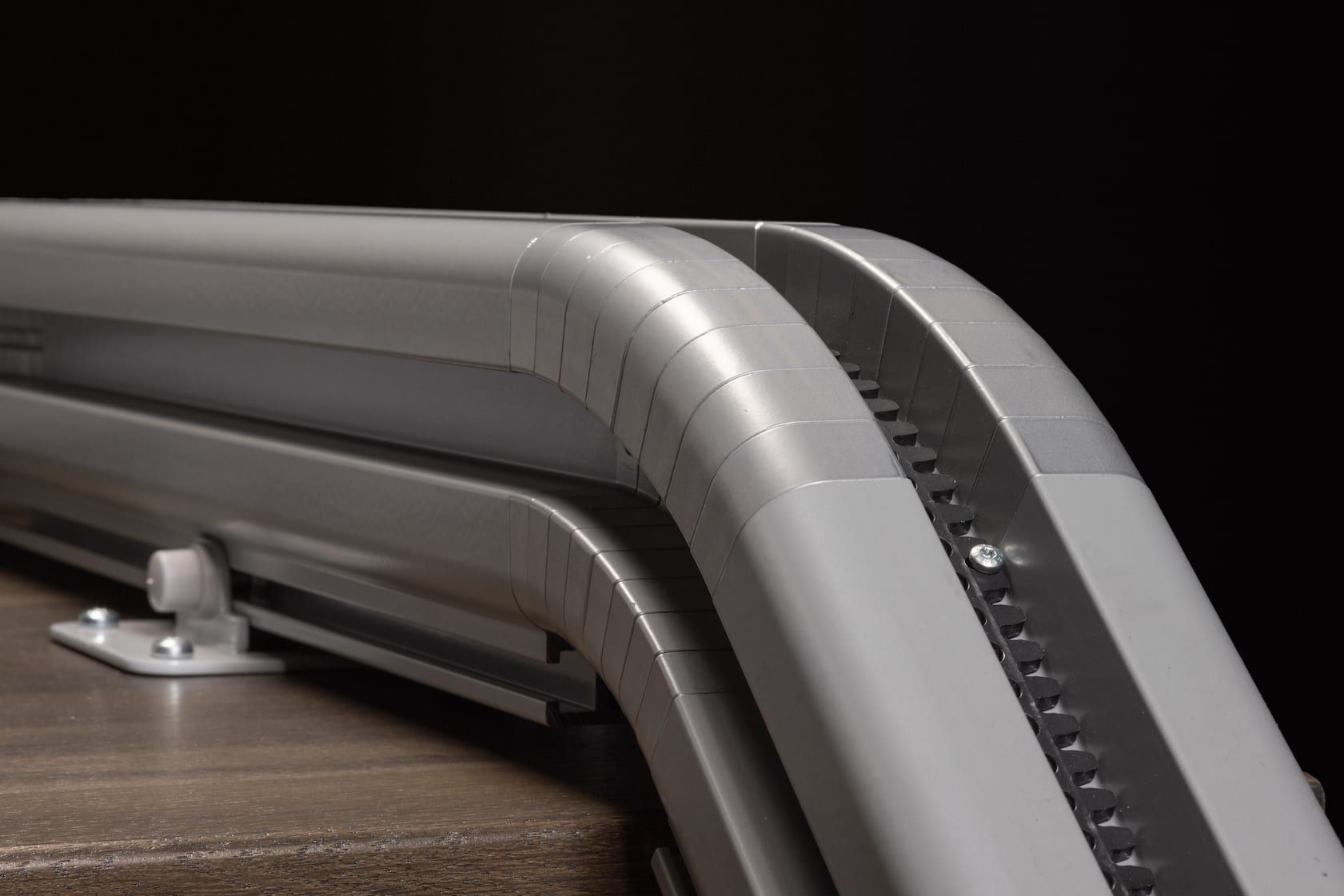 Close-up of a silver metal staircase handrail with a dark textured insert and black background