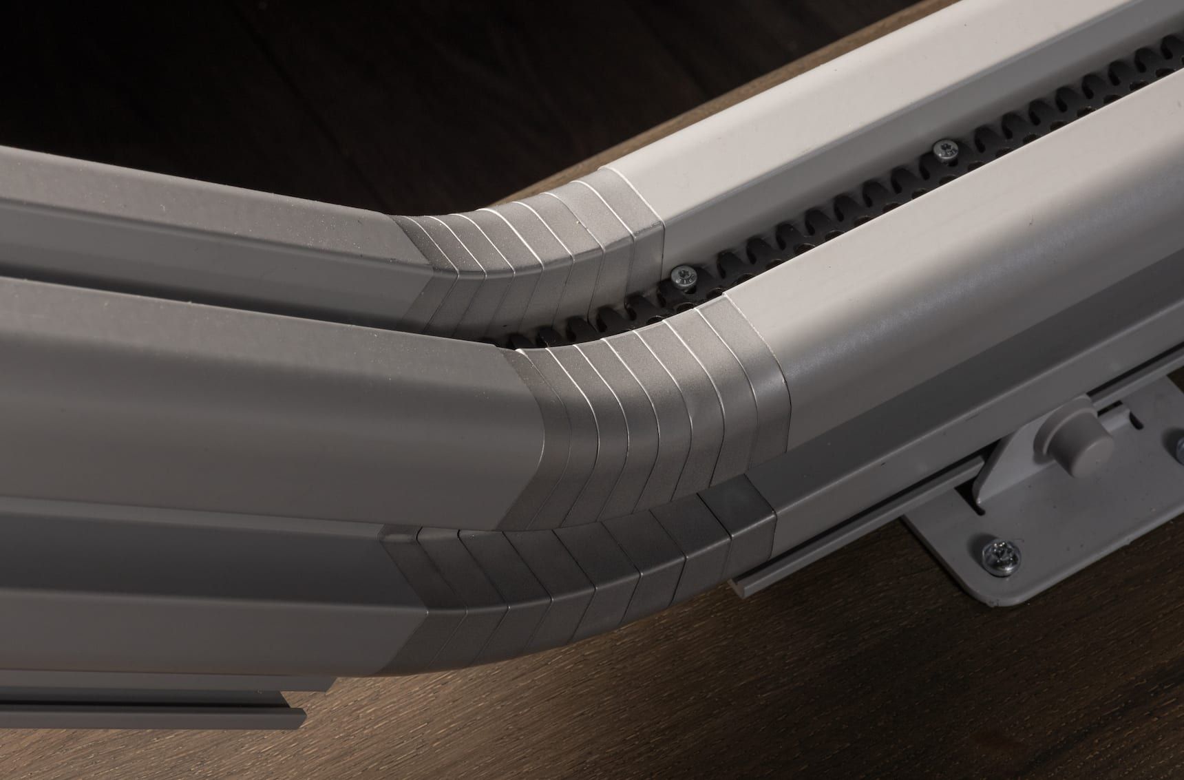 Close-up of a gray hard-shell suitcase corner with zipper tracks and a latch on a dark floor
