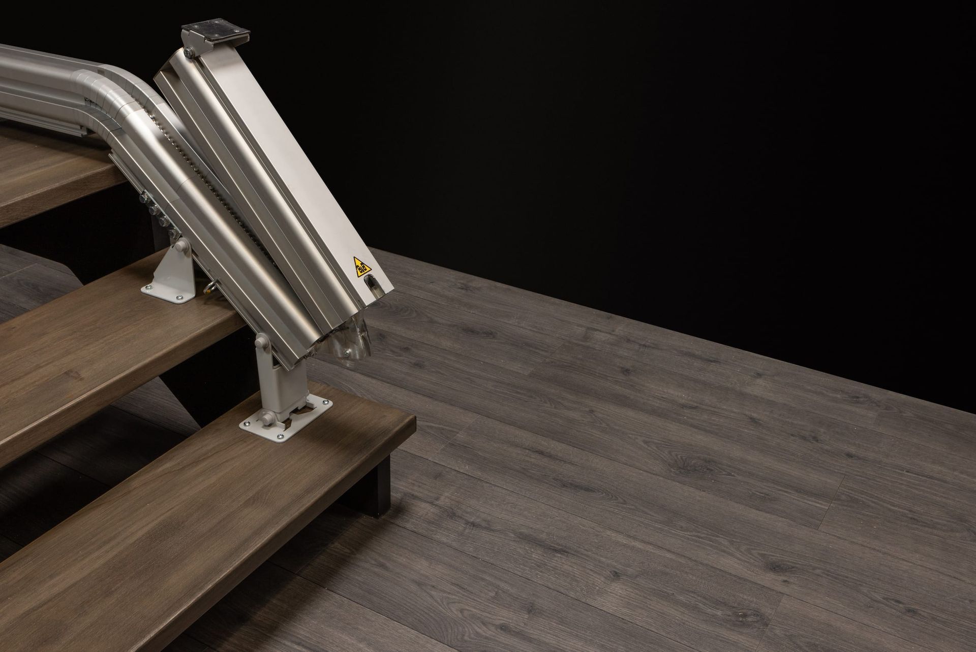 Metal stair lift on wooden stairs beside a gray floor against a black wall