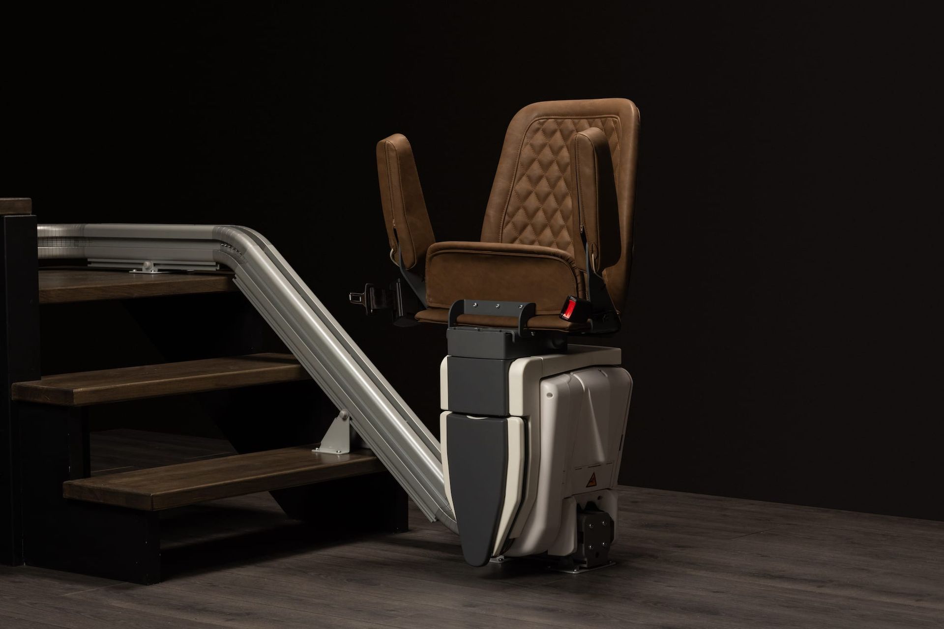 Modern chairlift with tan seats and silver railings in a dark indoor setting