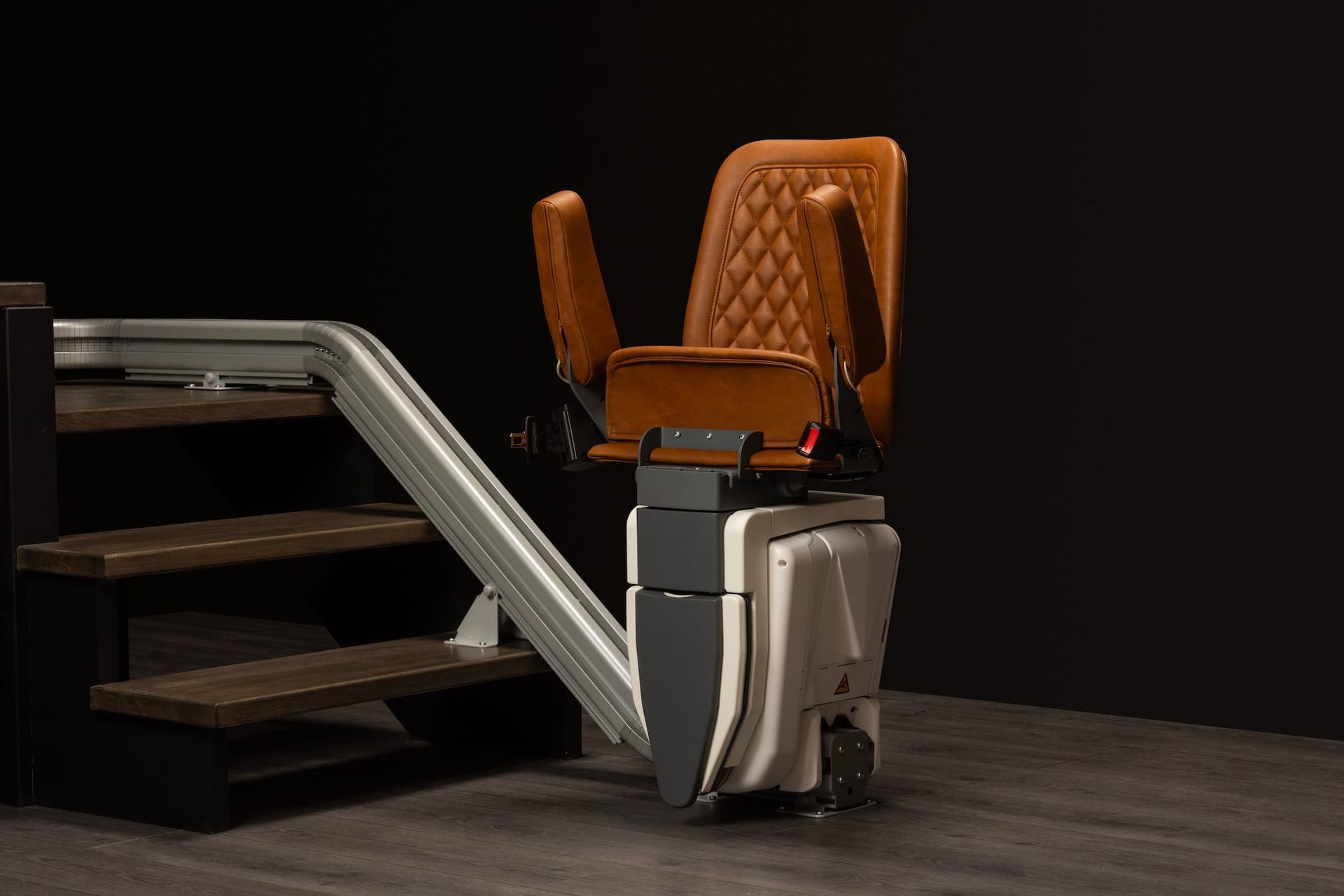 Vintage-style chairlift or stair lift with orange seat and silver rails on a dark floor against black background