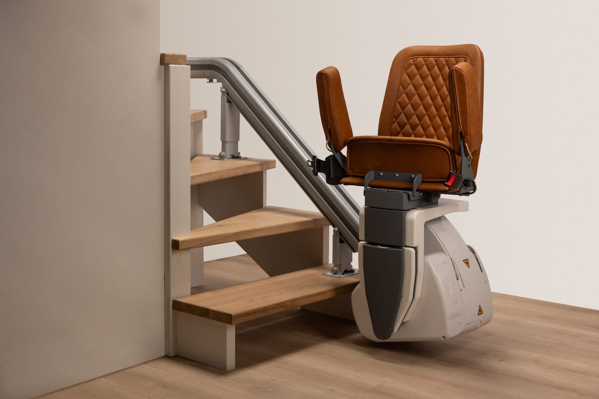 Brown stairlift installed on a small indoor staircase with wooden steps and beige walls.