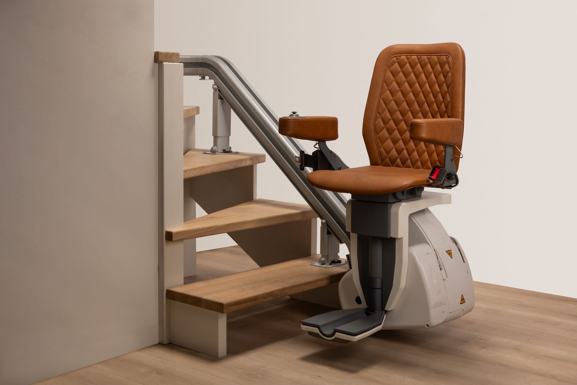 Compact stairlift with tan seat and silver frame installed on a wooden staircase indoors