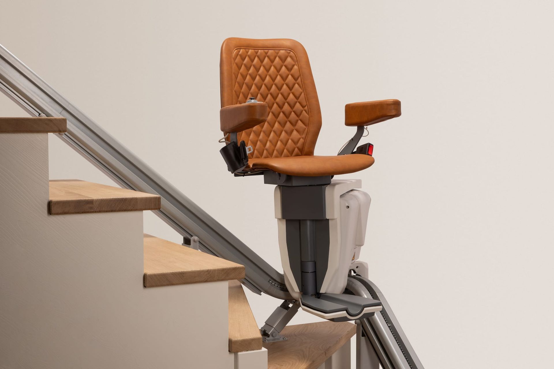 Orange stairlift on a staircase with metal handrails and wooden steps