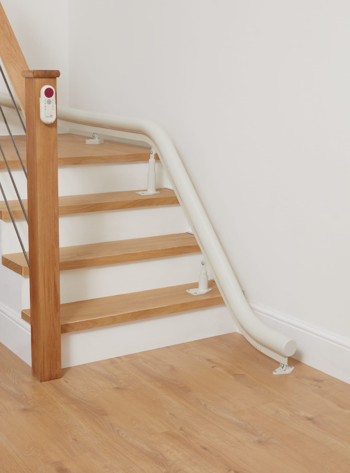 Staircase with wooden steps and a white chair lift handrail for accessibility. Light wood floor.
