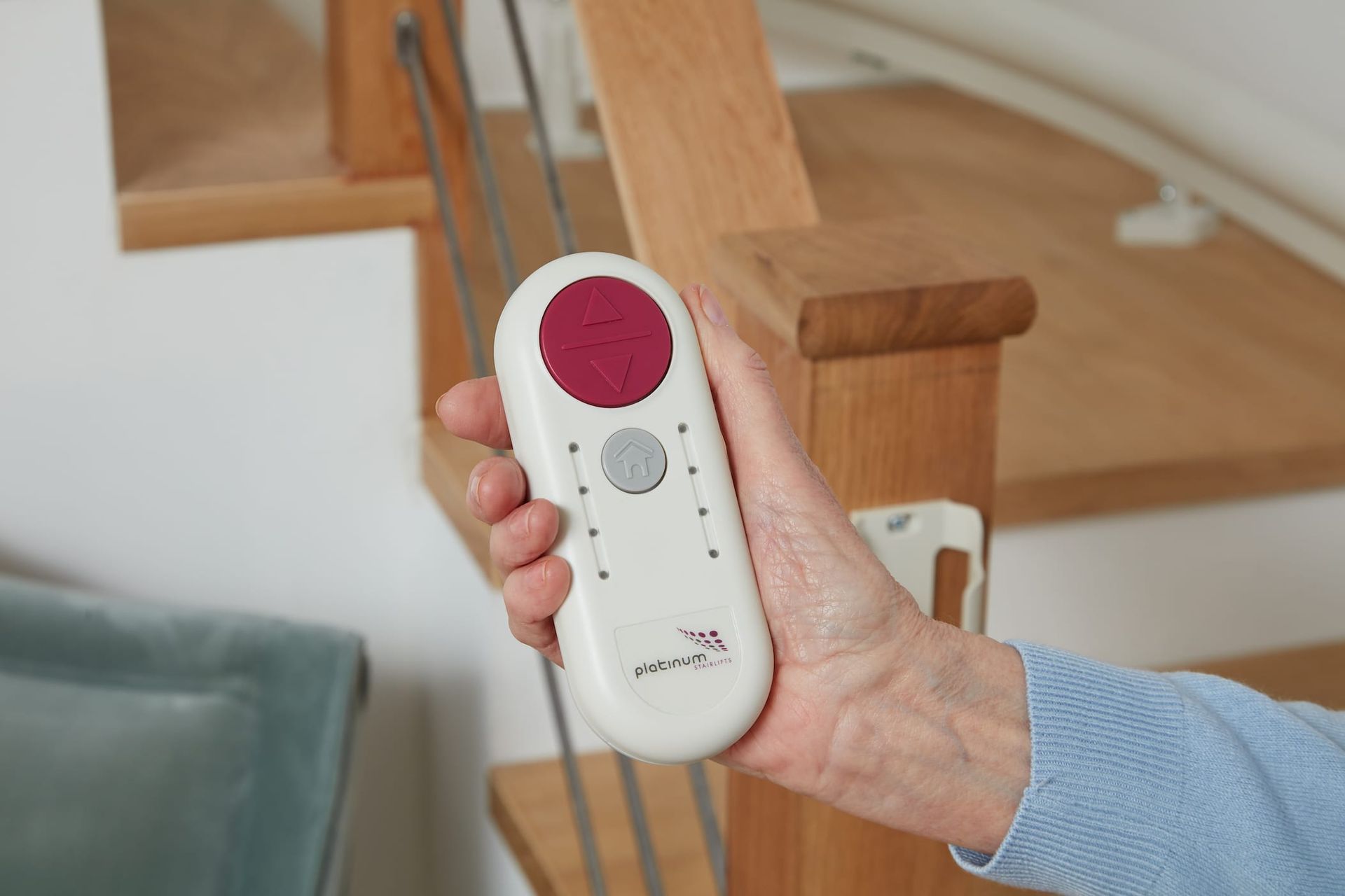 Hand holding a white remote with red and gray buttons near a staircase.
