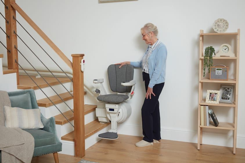 An older person standing next to a stair lift installed on a wooden staircase in a home.