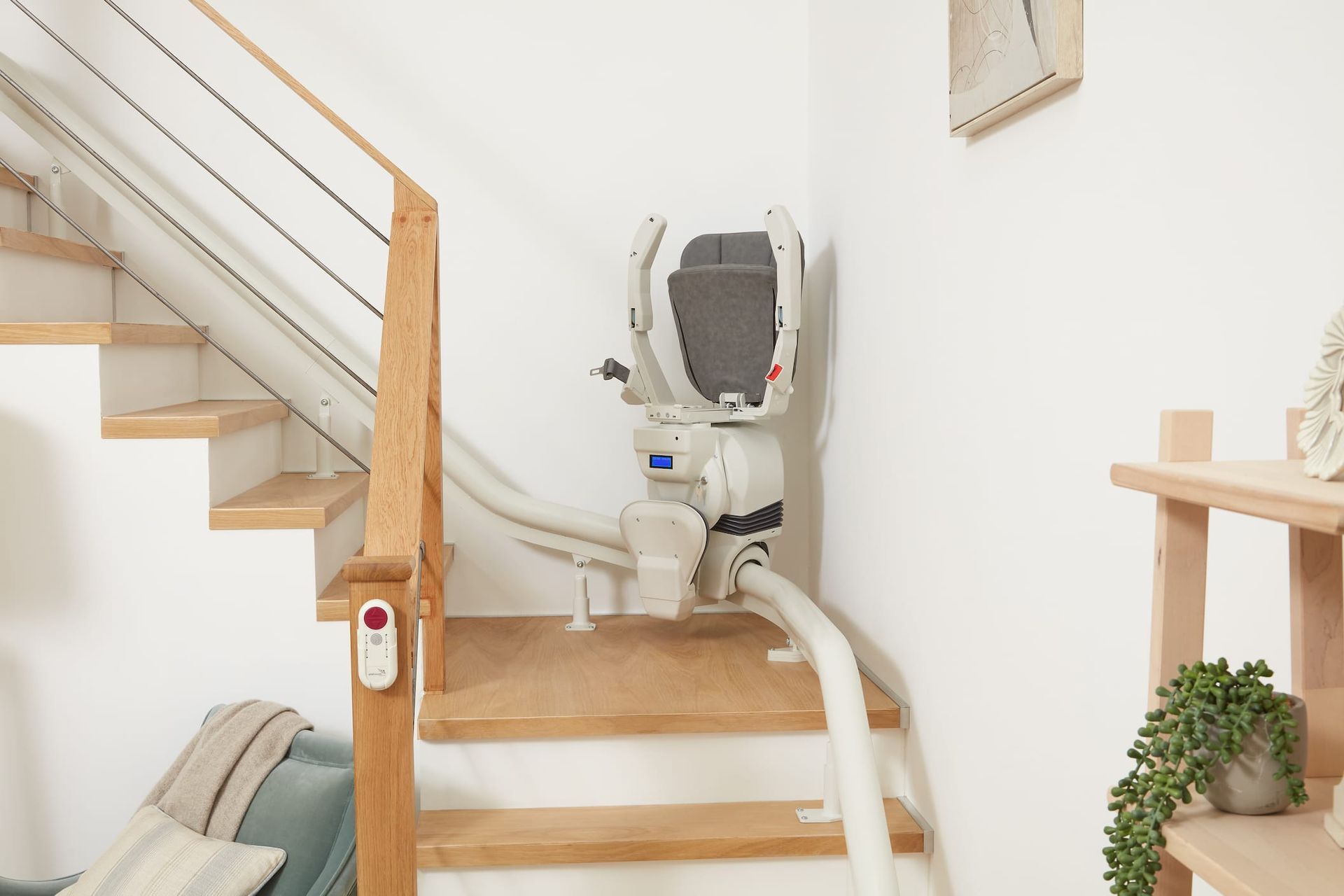 Stairlift on wooden stairs against a white wall; interior.