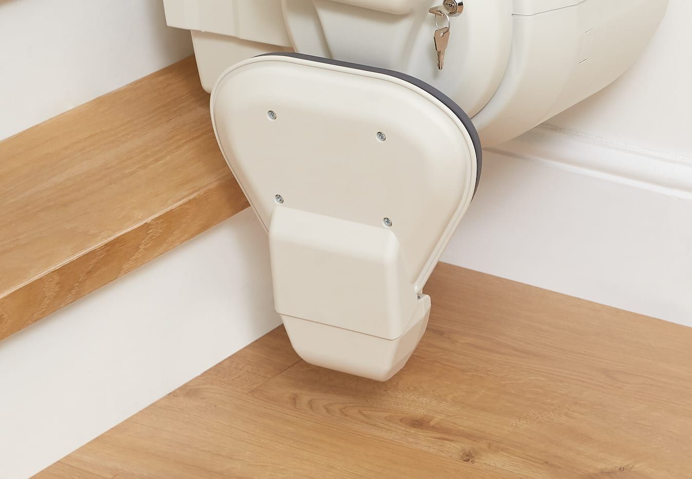 Beige stairlift footrest on light wood floor and step.