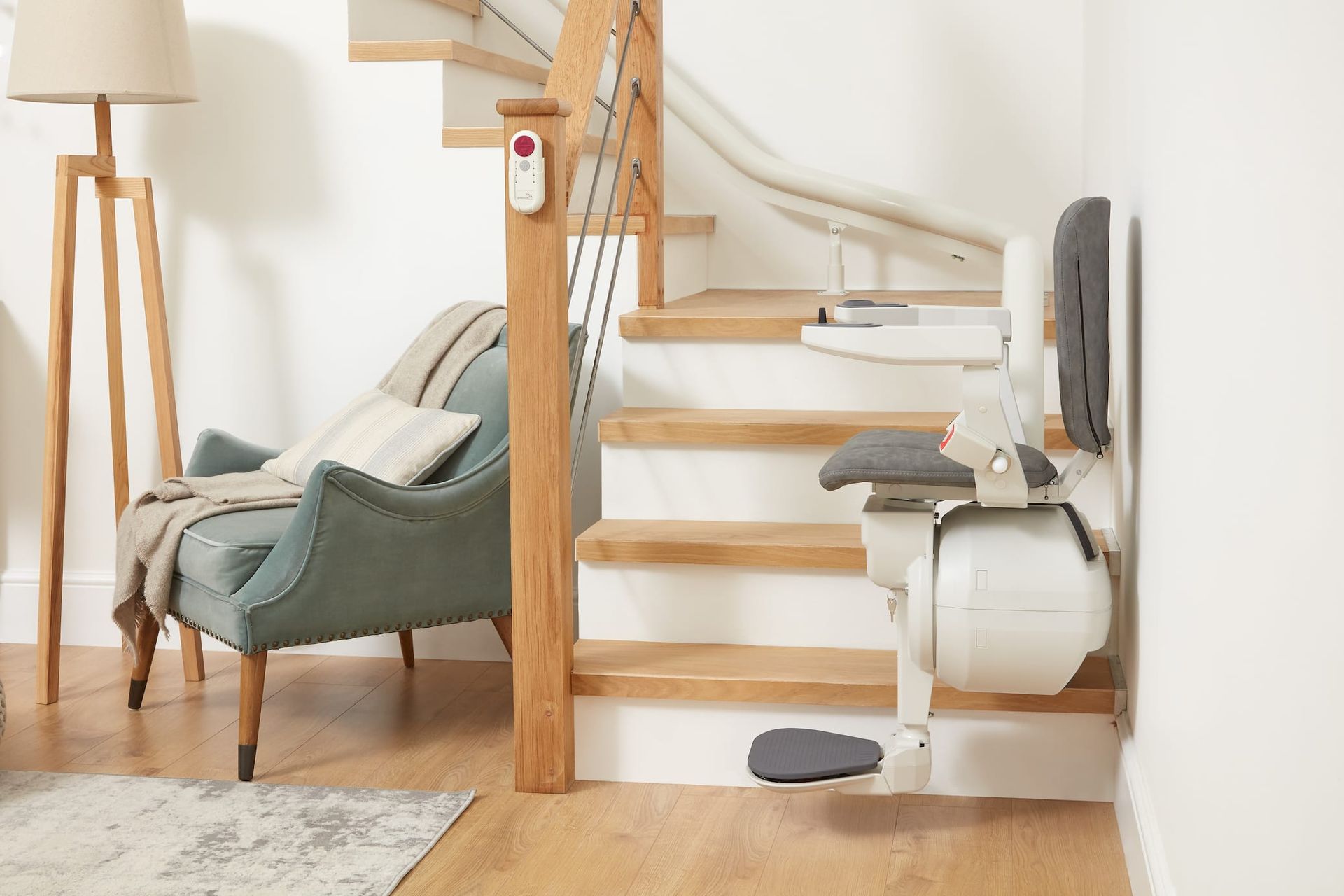 Stair lift installed on wooden staircase; chair and footrest are folded up against the wall.