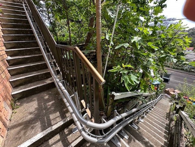 Outdoor stairway with metal handrails beside a brick wall and dense green trees