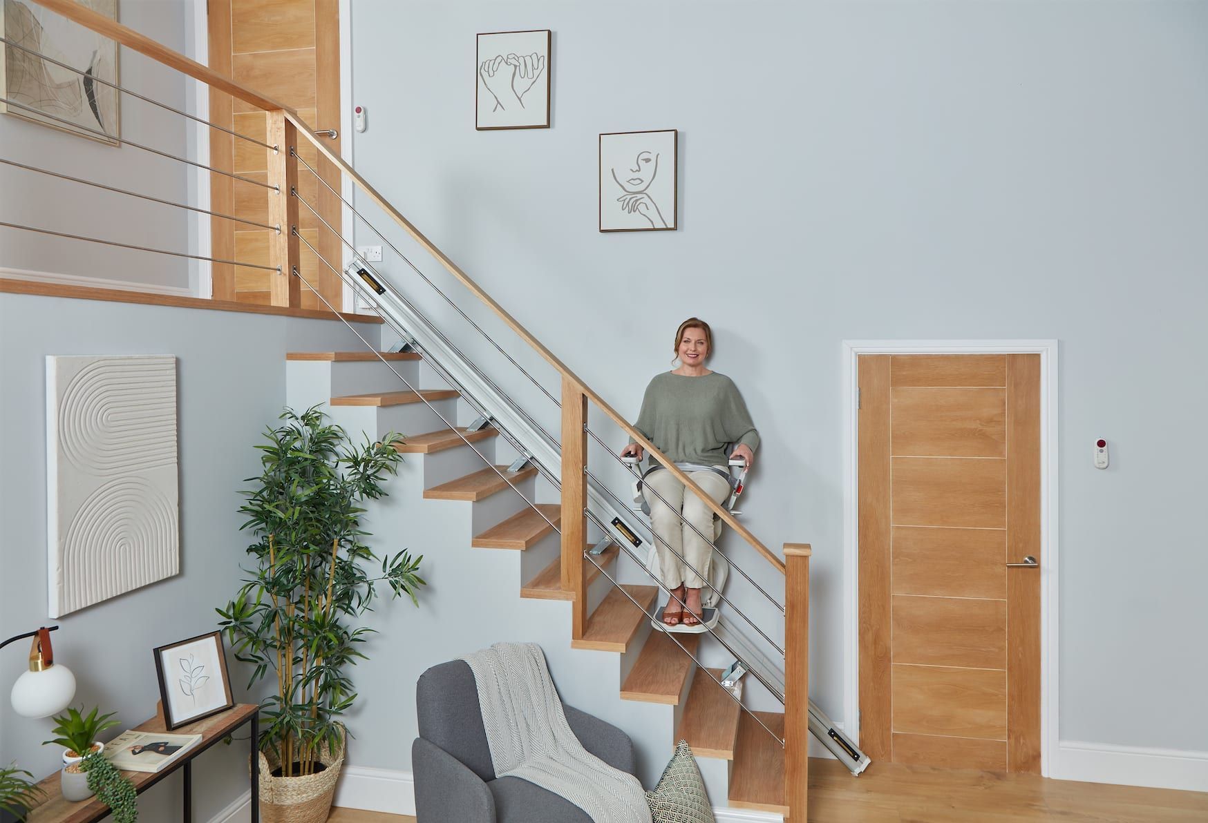 Person standing on a modern staircase in a bright living room with wood floors and a potted plant.