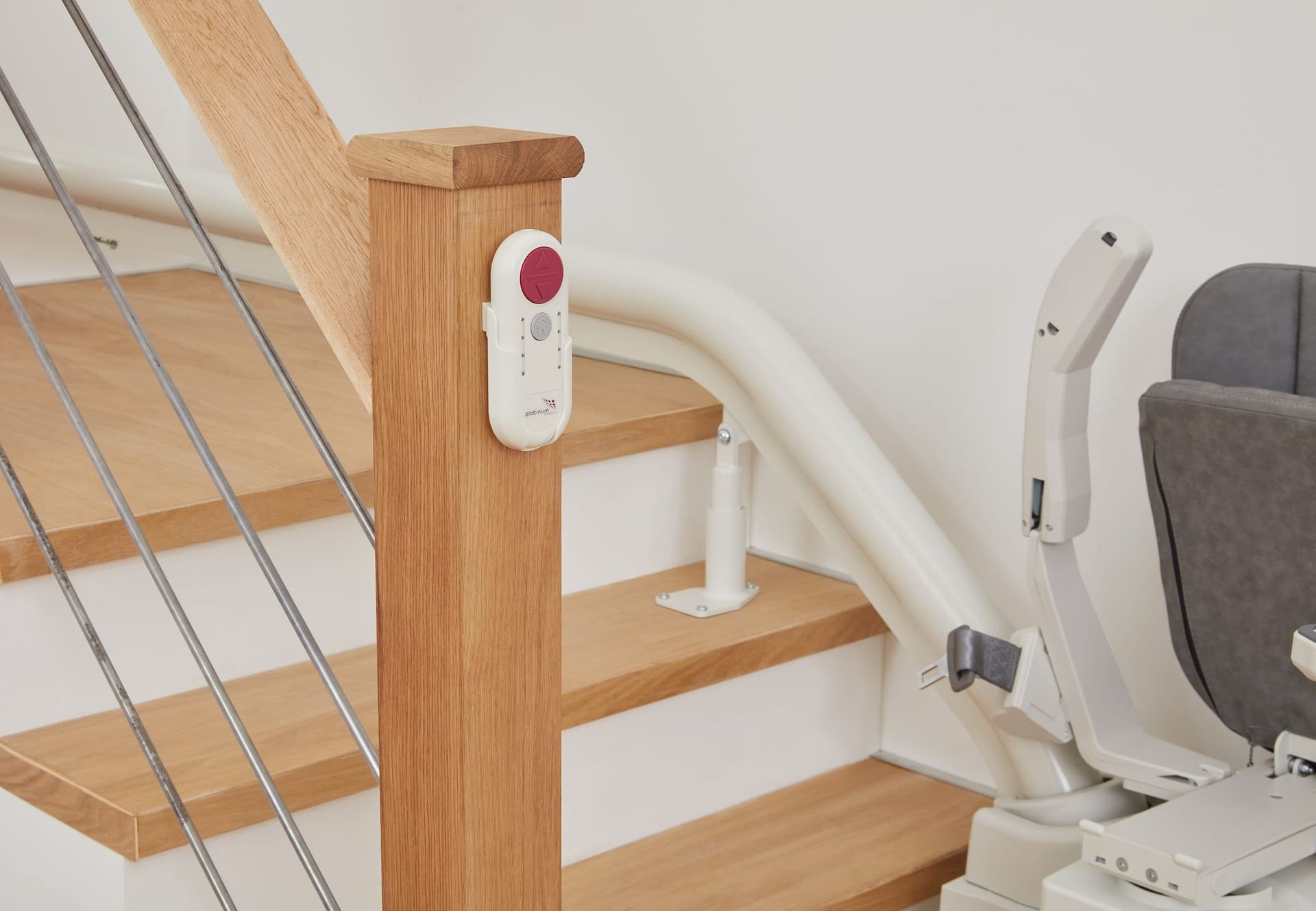 Stairlift on wooden stairs with handrail and wall-mounted remote control.