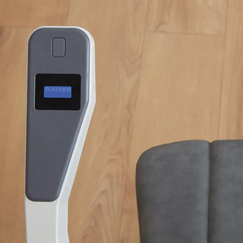 A close-up view of a gray control panel with a small digital display and button on a white stand over a wood floor.