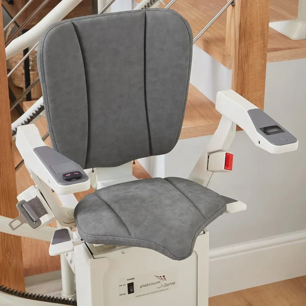 Woman on a stairlift smiles, ascending a wooden staircase beside a white wall.