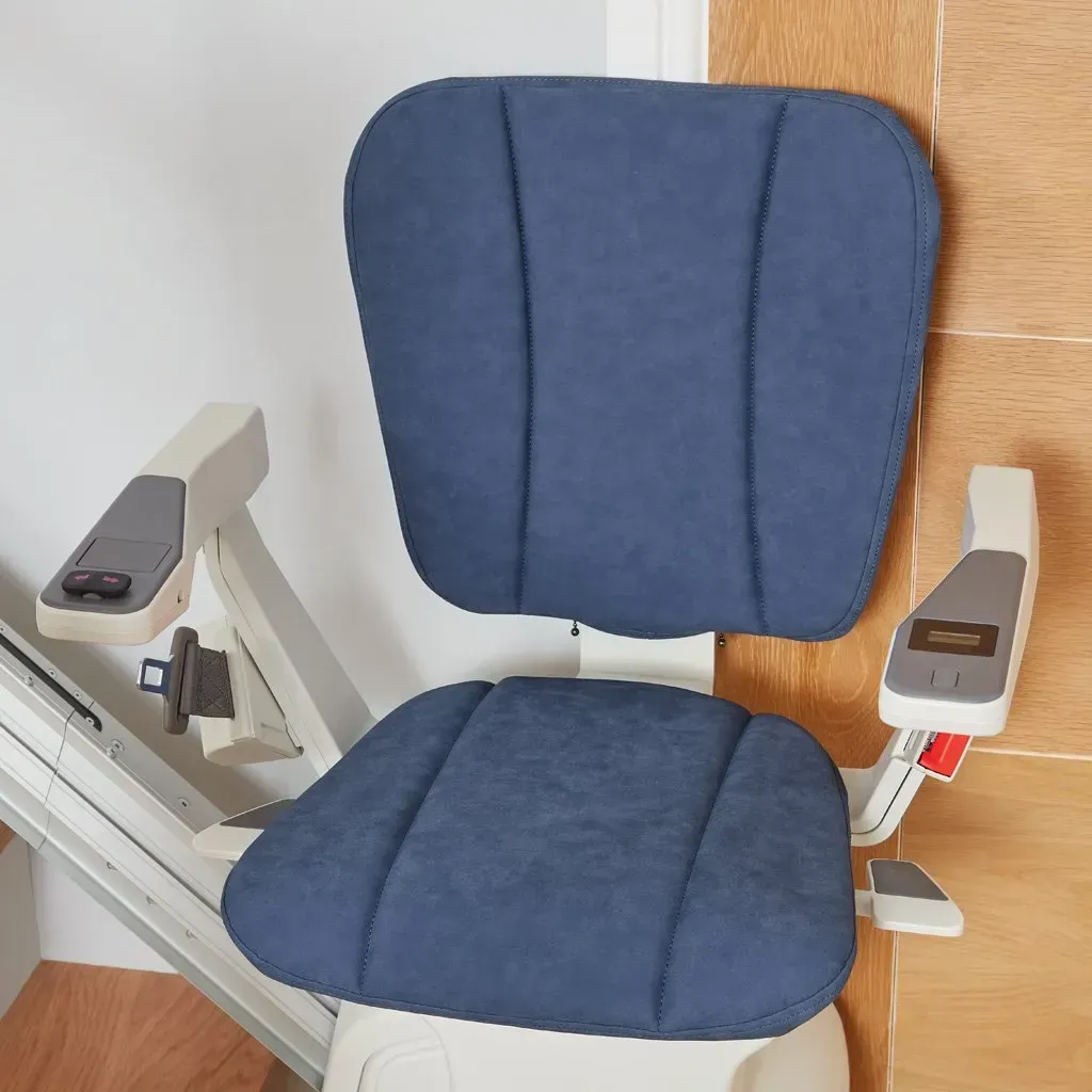 A blue upholstered stairlift chair with armrest controls, positioned on a rail alongside a wall.