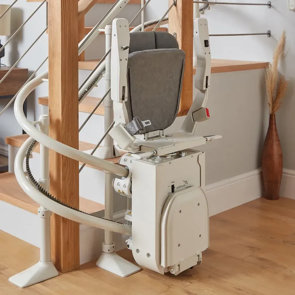 A white, motorized curved stairlift parked at the base of wooden stairs in a home.