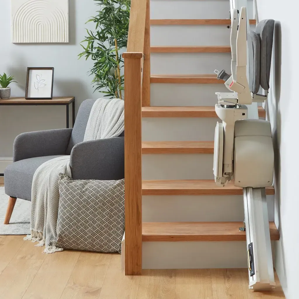 A white, motorized curved stairlift parked at the base of wooden stairs in a home.
