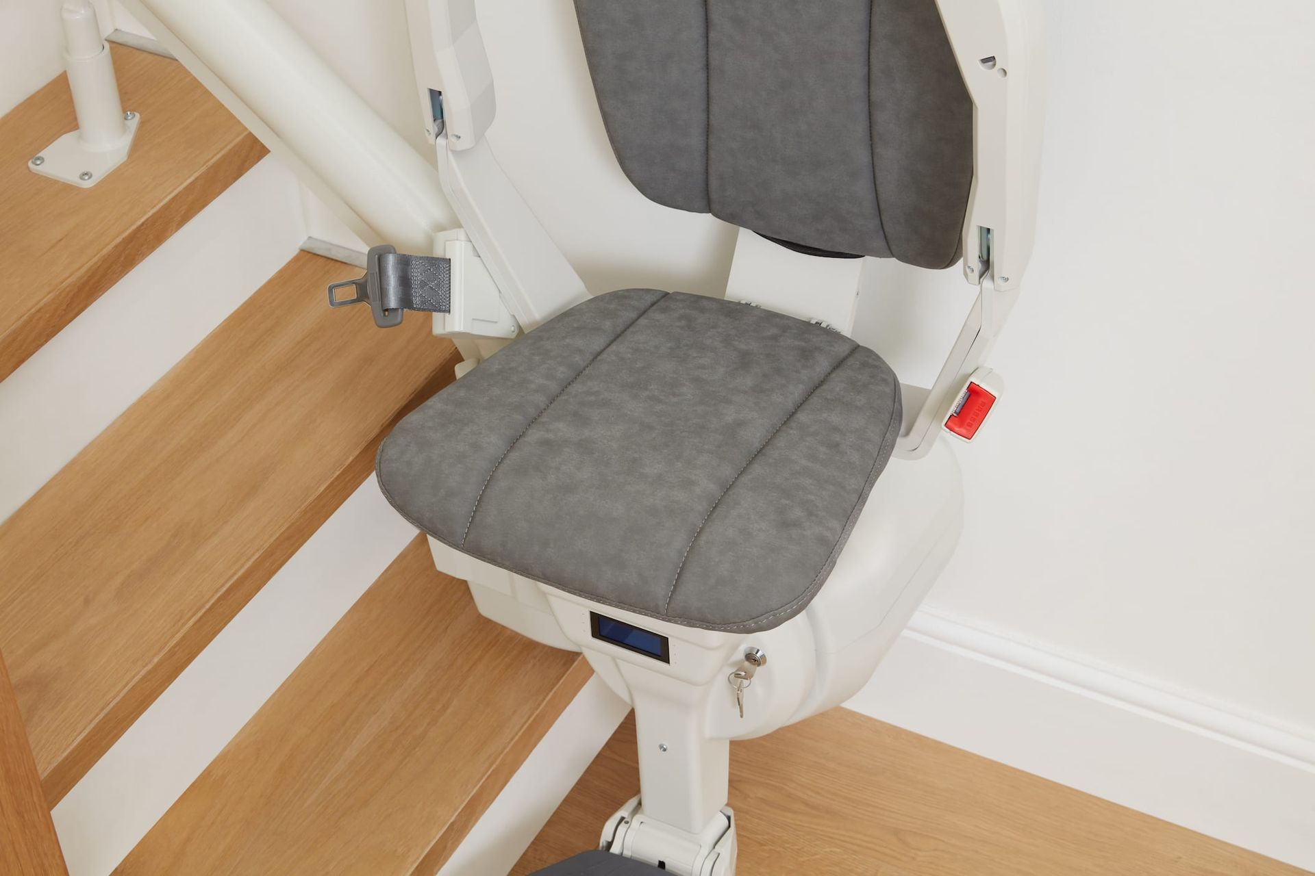 Stair lift chair with gray upholstered seat on wooden stairs, white railing, and wall.