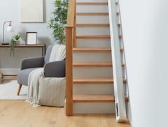 Minimalist room with a wooden staircase, gray chair, and indoor plants beside a white wall