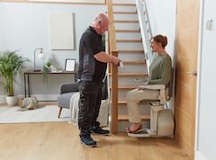 A man helping a seated person operate a stair lift in a bright home hallway