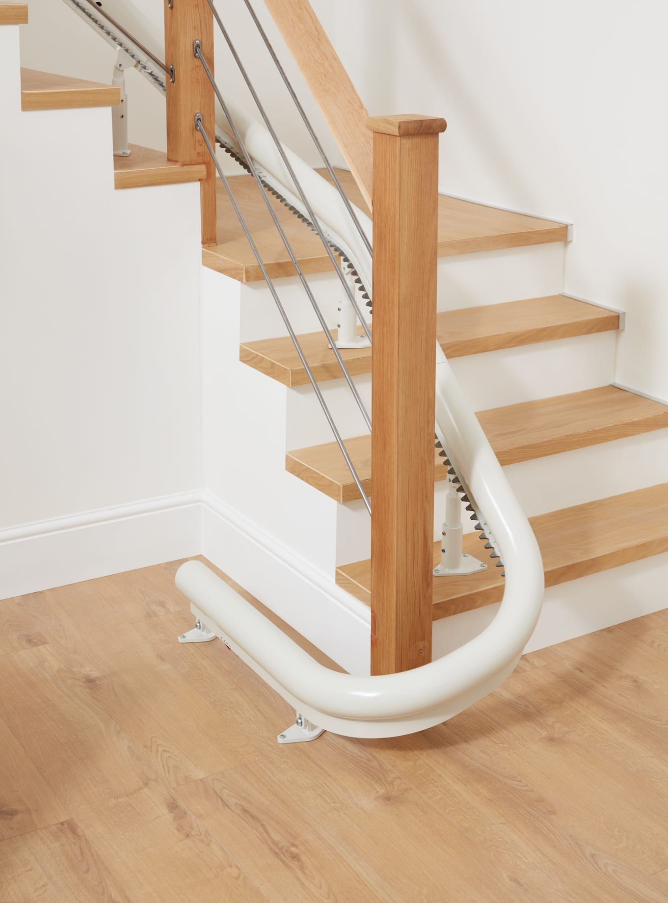 Stairlift on wooden stairs with white walls and flooring.