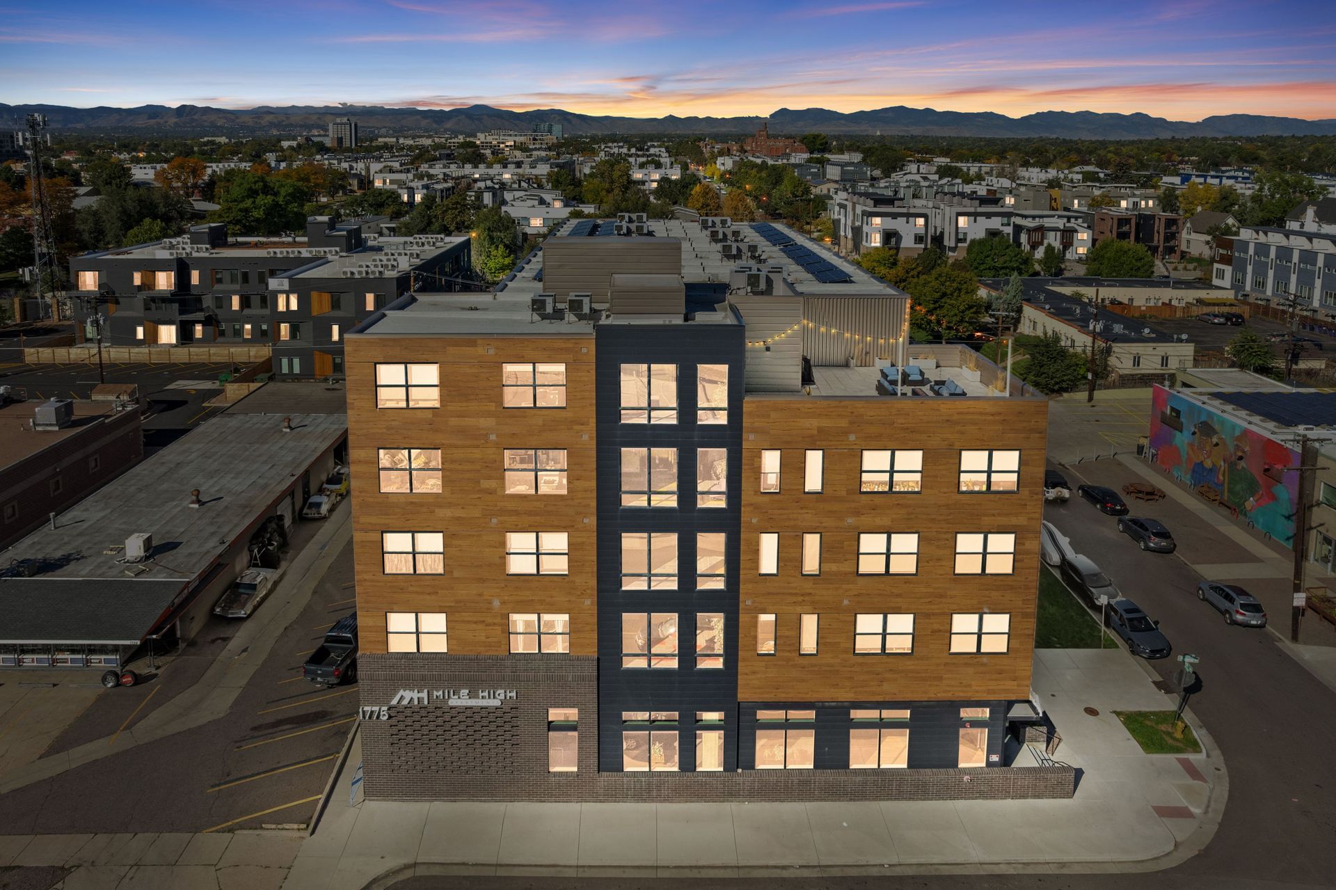 Modern multi-story building at dusk with illuminated windows and surrounding buildings.