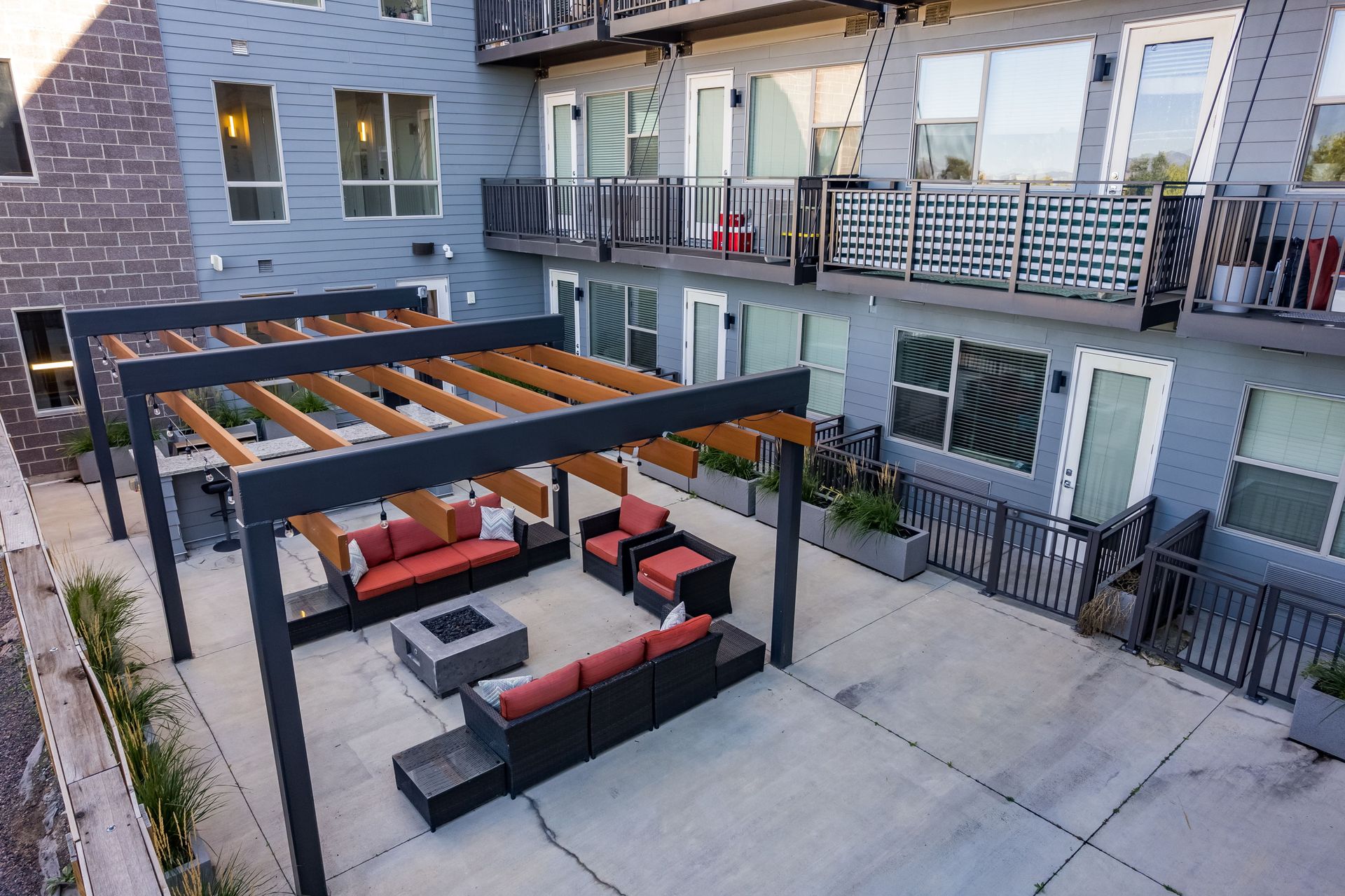 Outdoor patio with seating, fire pit, and pergola; gray building in background.