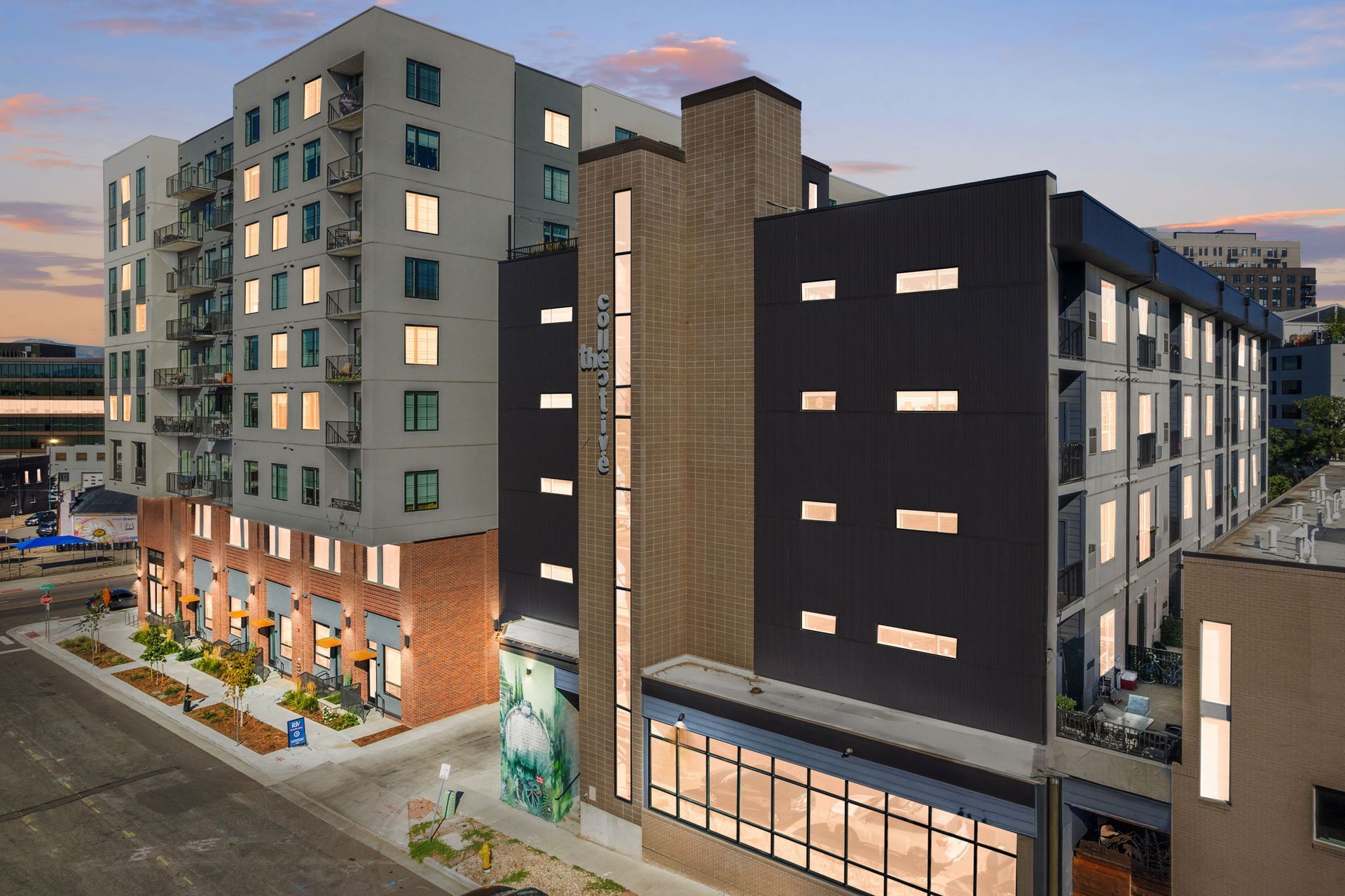 Modern multi-story apartment complex at dusk, with lit windows and storefronts.