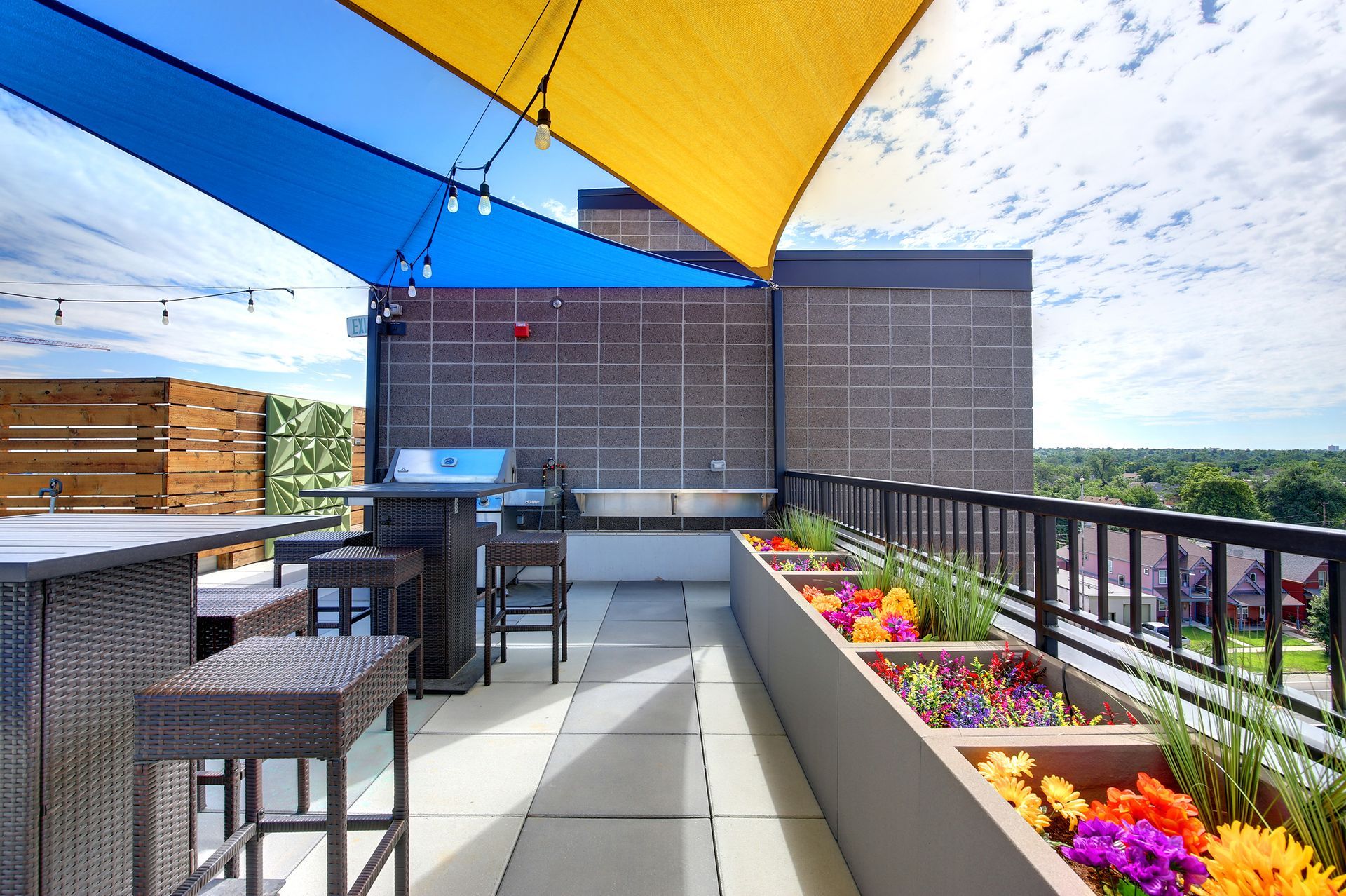 Rooftop patio with a grill, seating, shade sails, and a colorful flower box.