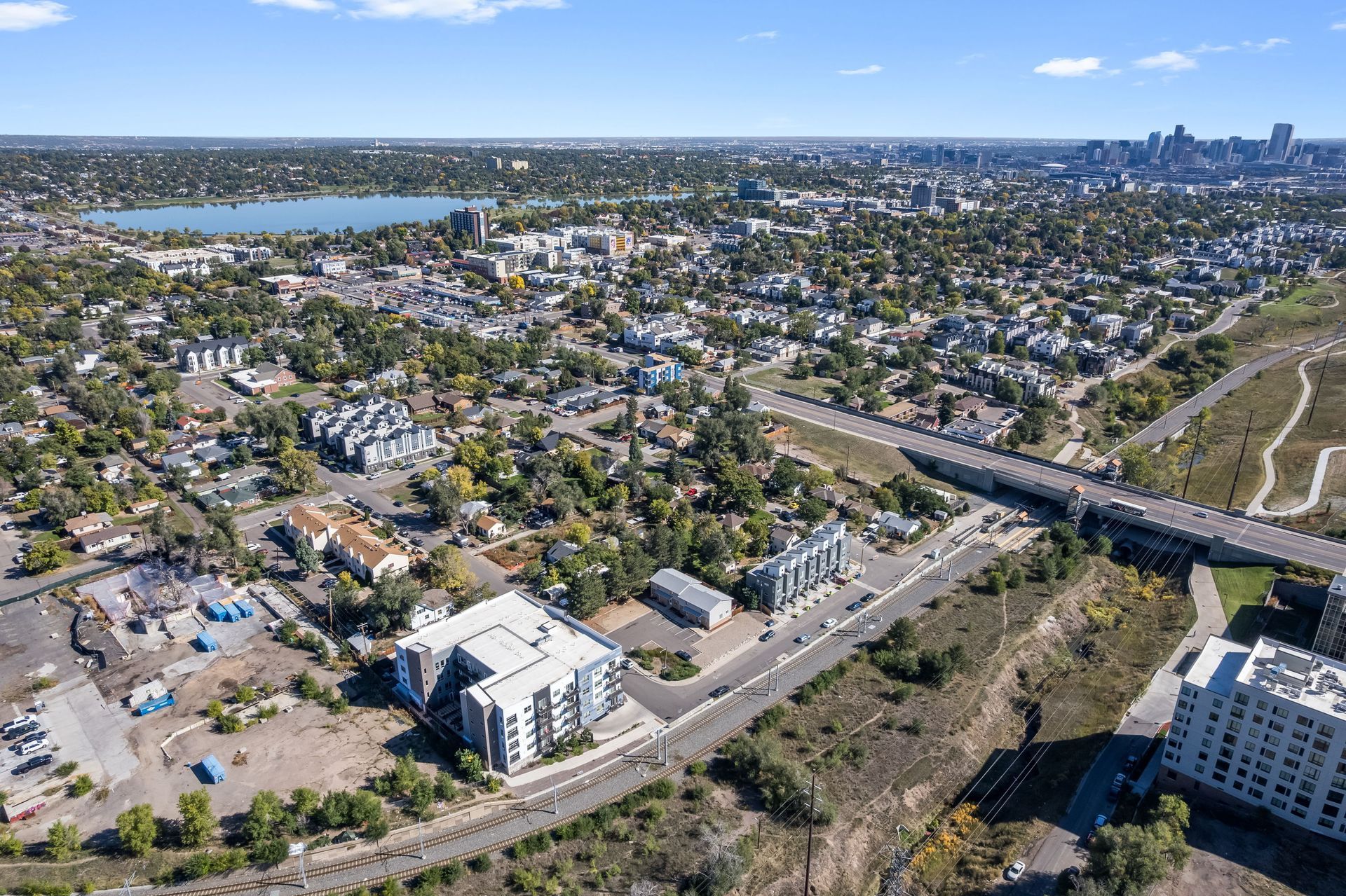 Aerial view of a city with a lake and highway visible. Buildings, trees, and blue sky.