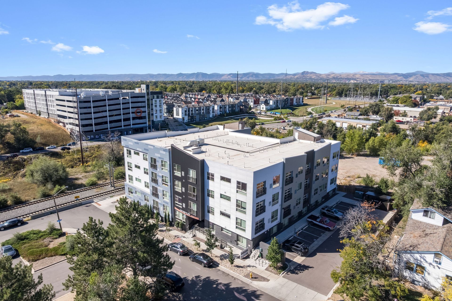 Modern apartment building with a flat roof, surrounded by trees and other buildings.