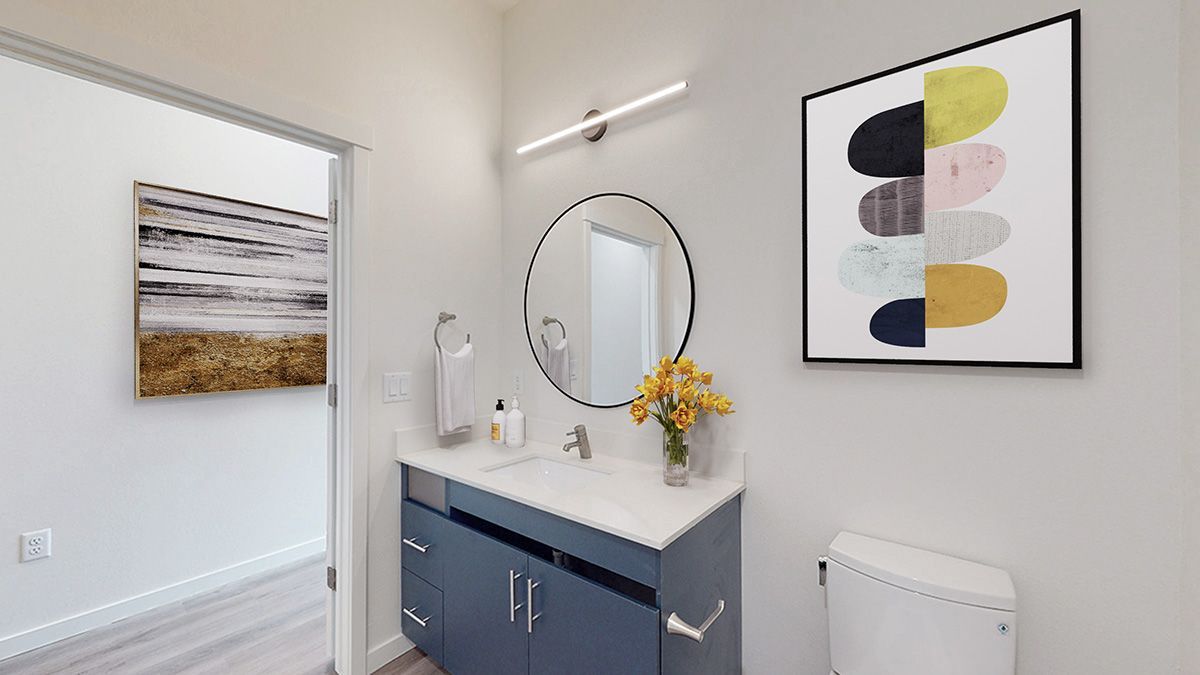 Modern powder room with blue vanity, round mirror, abstract art, and small flower arrangement.