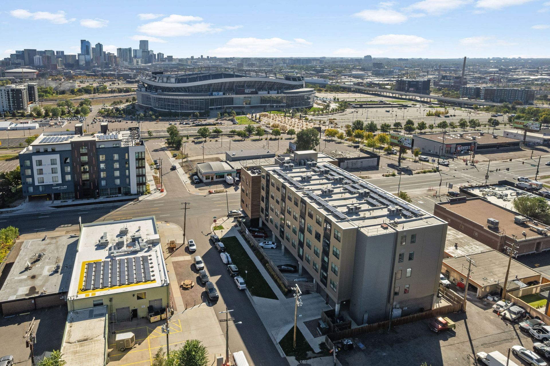 Aerial view of buildings in Denver, Colorado, with the city skyline and Empower Field at Mile High in the background.