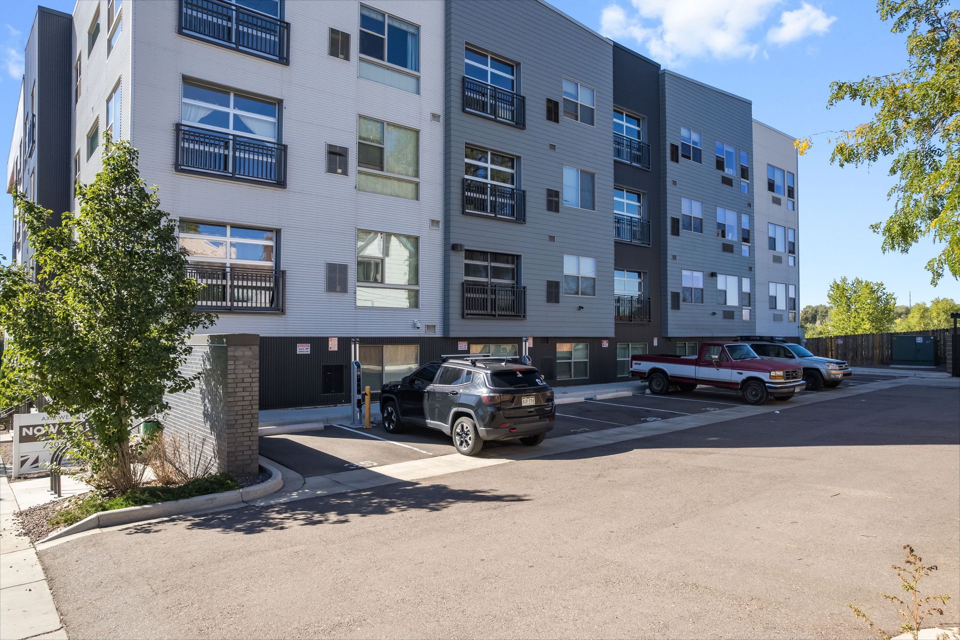 Modern apartment building with parked cars in front. Gray and white facade.